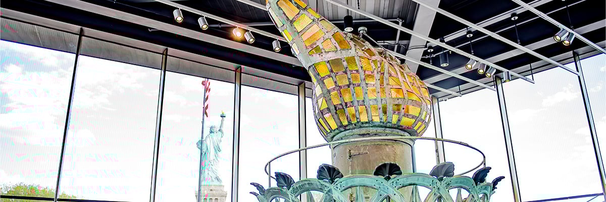 A model of the Statue of Liberty's torch with the back view of the Statue of Liberty in the background